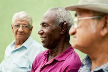 retired elderly people and free time, group of happy senior african american and caucasian male friends talking and sitting on bench in park